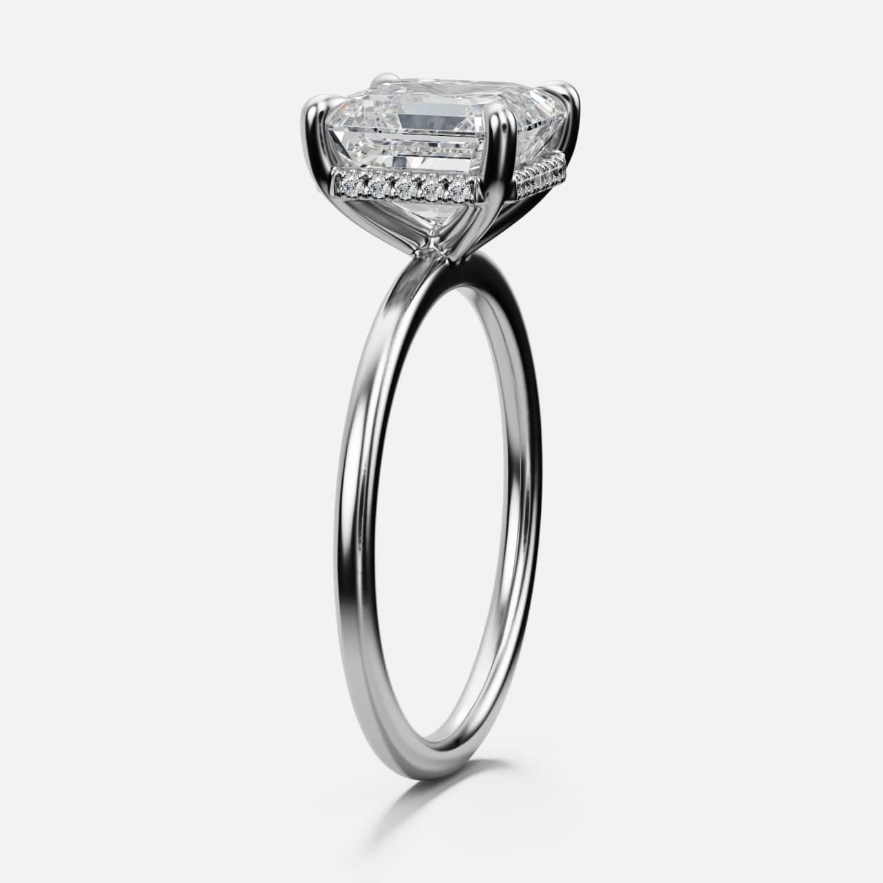 Three-quarter view of a white gold emerald-cut diamond solitaire with double-claw prongs and a hidden halo on a thin band