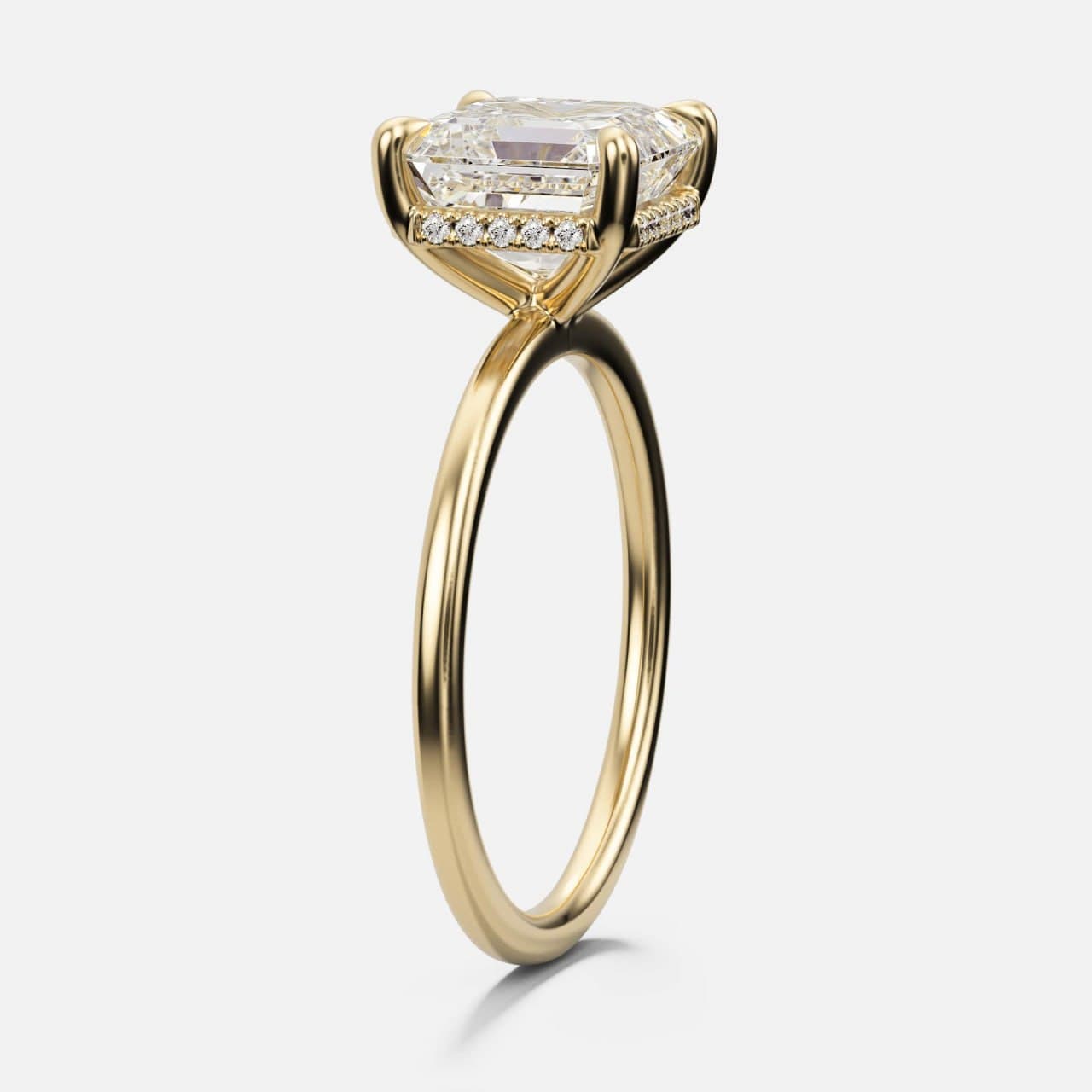 Three-quarter view of a yellow gold emerald-cut diamond solitaire on a knife-thin band with double claws and a hidden halo