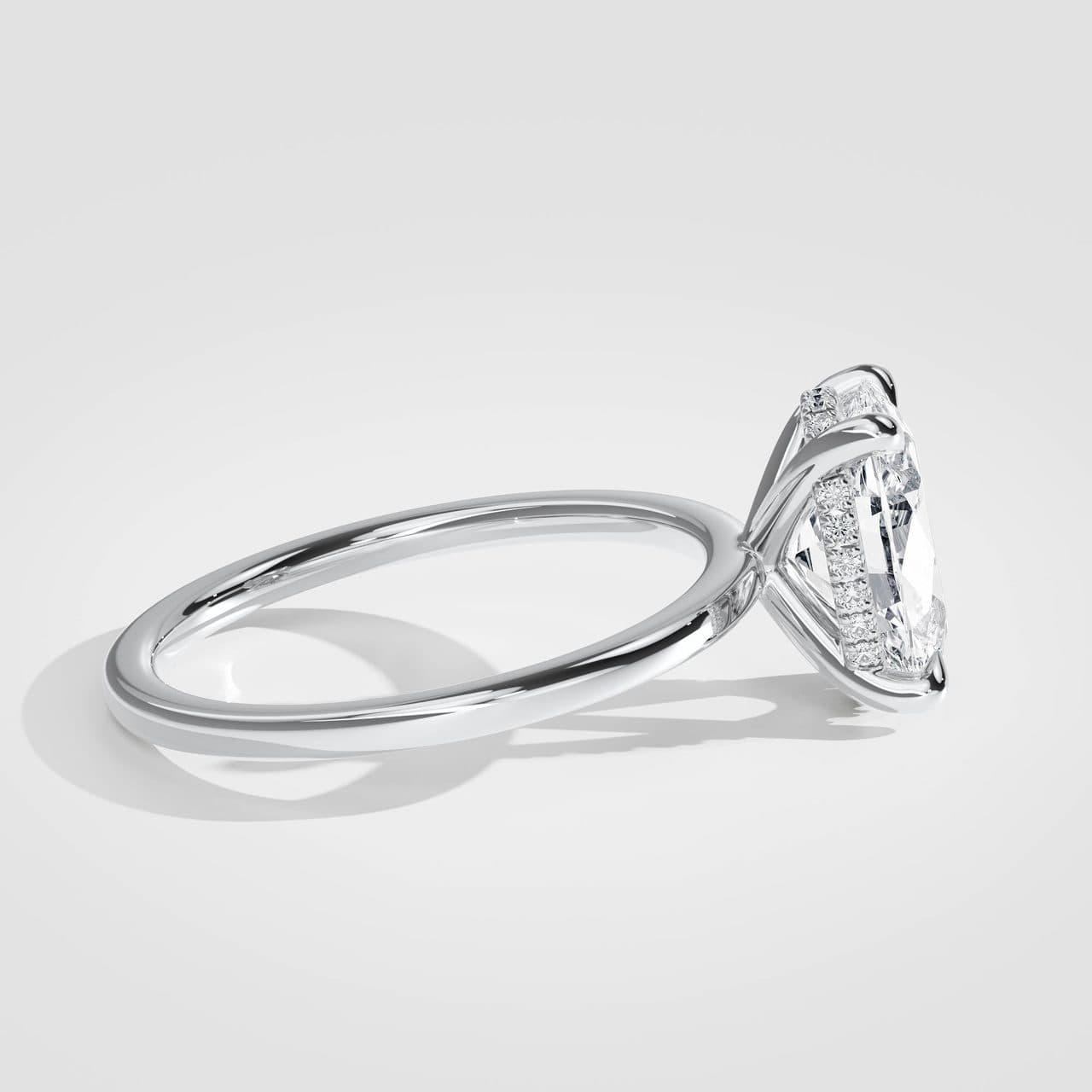 Side view of a white gold oval solitaire lying on a pale surface, a long bright highlight running along the polished band