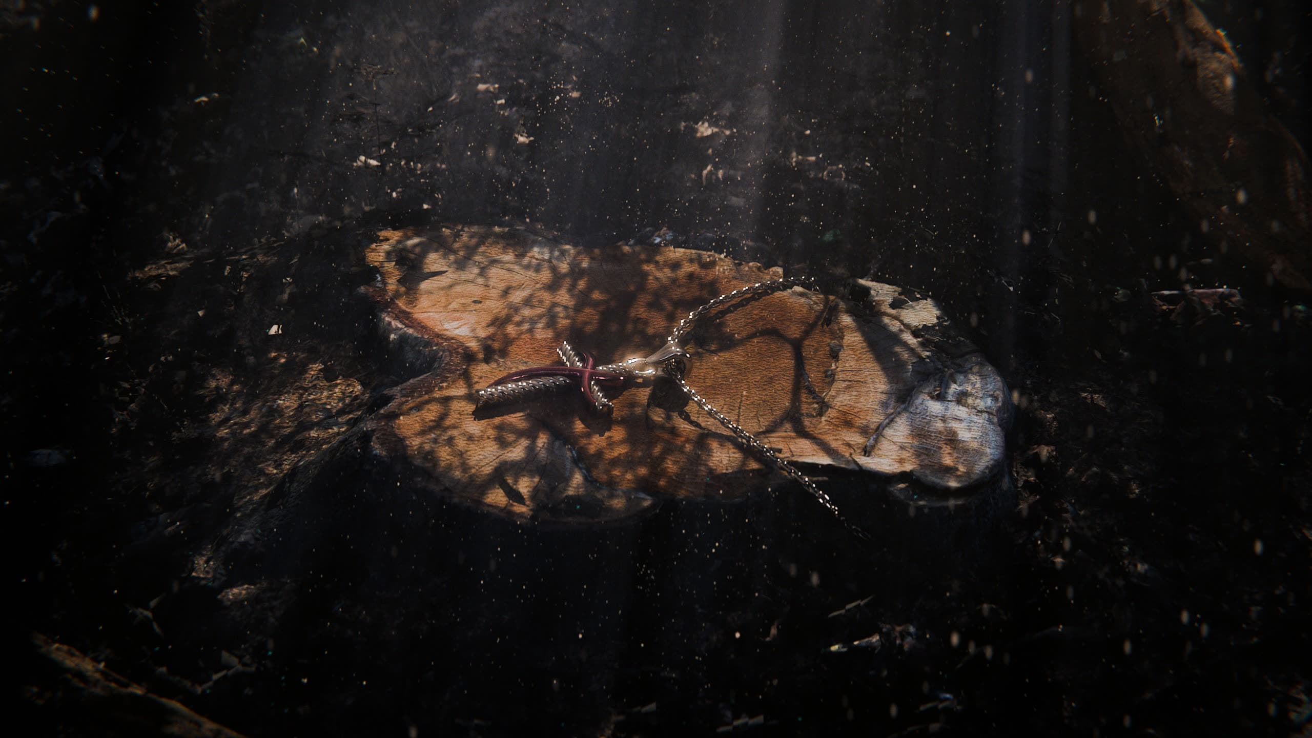 A silver pendant on a weathered tree stump in a dark, cinematic forest with god rays and drifting dust — the free Blender dark forest render studio scene by 4rend Studio